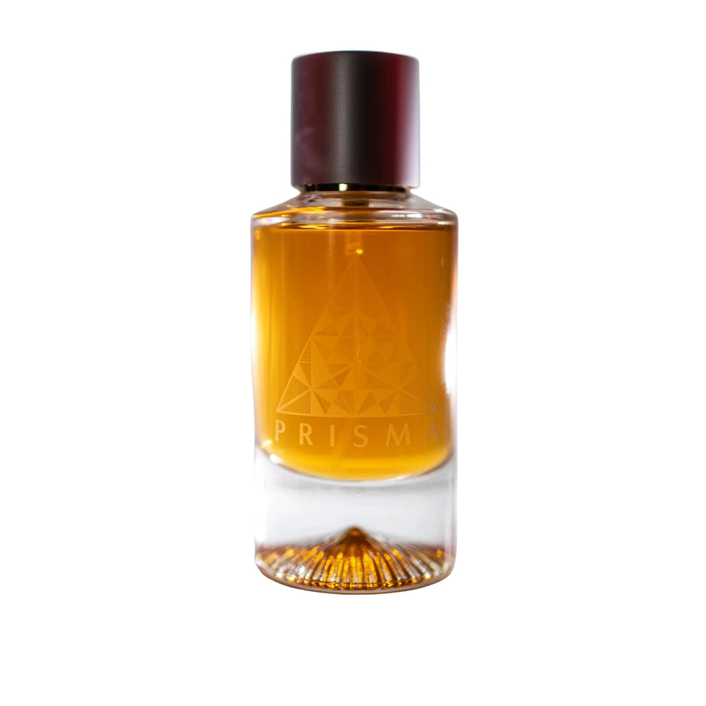 A clear glass perfume bottle filled with amber-colored liquid, featuring a faceted geometric design and a dark brown cap. The brand name 'PRISMA' is embossed on the front of the bottle.