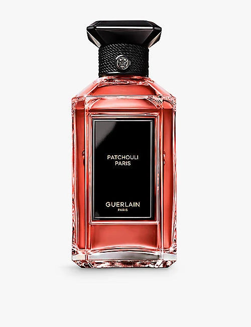 Guerlain Patchouli Paris perfume bottle with a faceted clear glass body showing a pinkish-red liquid, a black label, and a black cap with a silver brand emblem, on a light gray background.